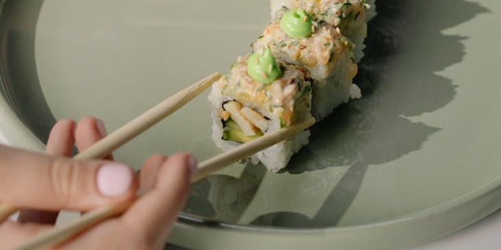 A person with chopsticks eating sushi from a plate at a sushi restaurant.