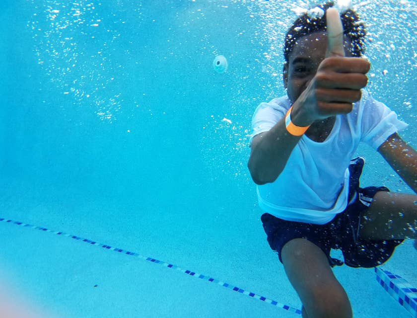 Un garçon lève le pouce tandis qu'il apprends à nager dans une école de natation.