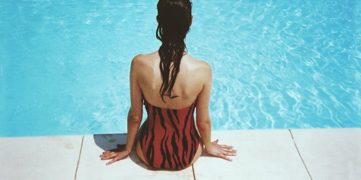 A woman wearing swimwear sitting on the side of a swimming pool.
