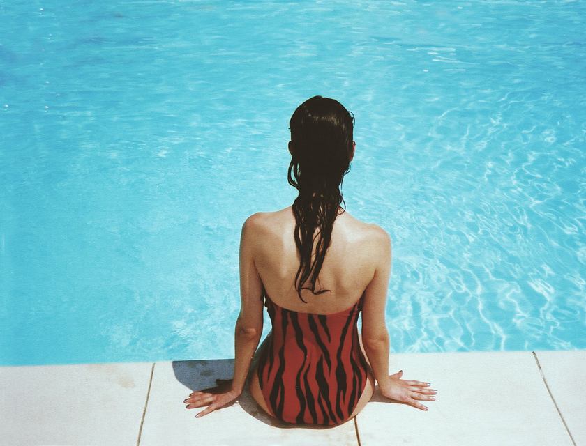Une femme en maillot de bain assise au bord d'une piscine.