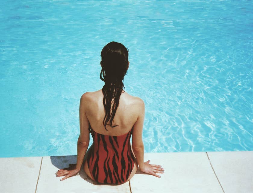 Une femme en maillot de bain assise au bord d'une piscine.