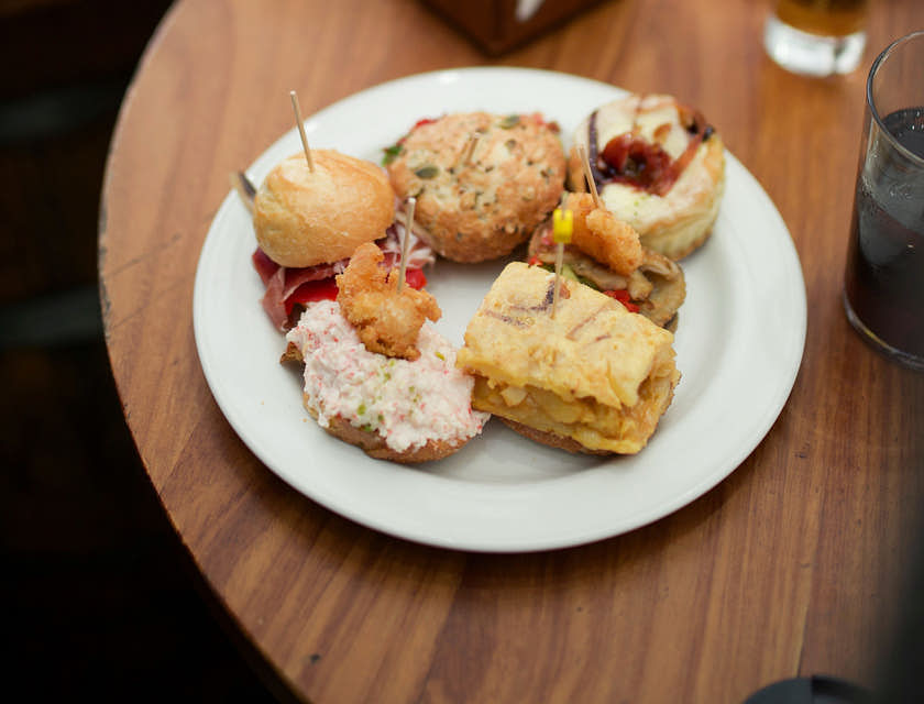 Due piatti di tapas serviti con delle bevande alcoliche sopra il tavolo di un tapas bar.