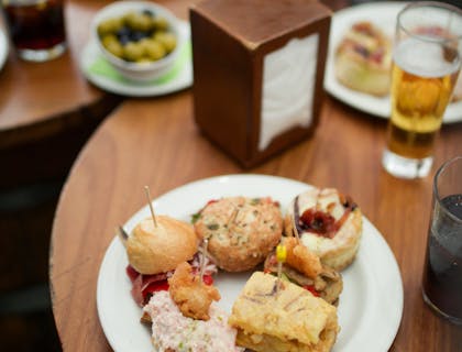 Due piatti di tapas serviti con delle bevande alcoliche sopra il tavolo di un tapas bar.