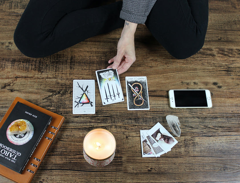 Une main touchant une carte de tarot à côté d'un livre, de bougies, photos, cristal et téléphone.