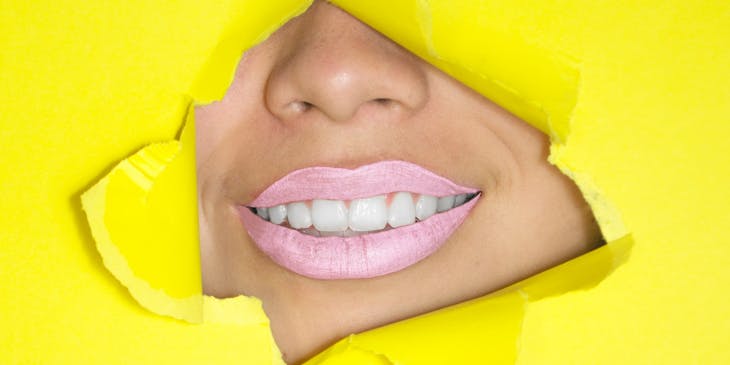 A smiling mouth with pink lipstick and white teeth.