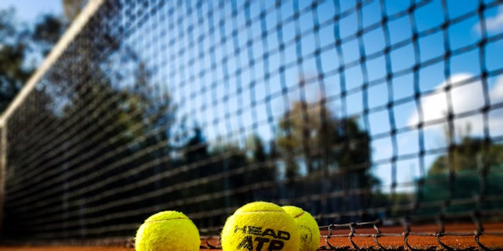 Tennis balls laying in front of a tennis net.