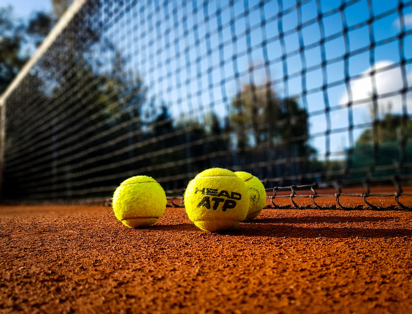 Tennis balls laying in front of a tennis net.
