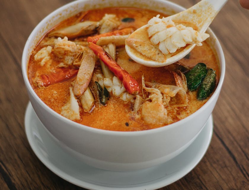 Sopa tailandesa de coco en un bowl de cerámica blanca sobre una mesa de madera