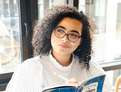 Una mujer que parece pensativa mientras toma notas en su libro.