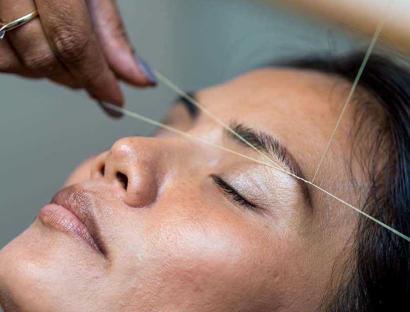 Una donna che si fa depilare le sopracciglia con la tecnica del threading o depilazione con filo.