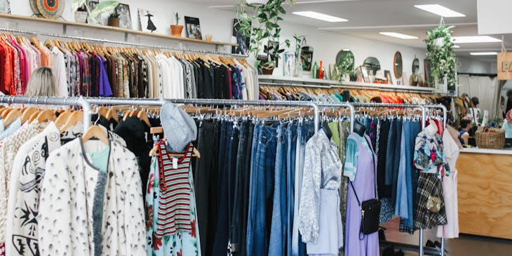 Assorted shorts, jeans, and skirts hanging in a well-lit store decorated with hanging and potted plants in a thrift store.
