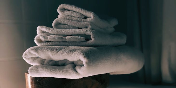 Three white towels folded on a stool in the bathroom.