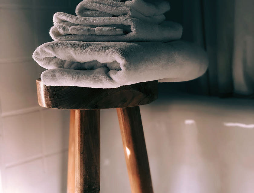Trois serviettes de bain blanches pliées sur un tabouret dans une salle de bain.
