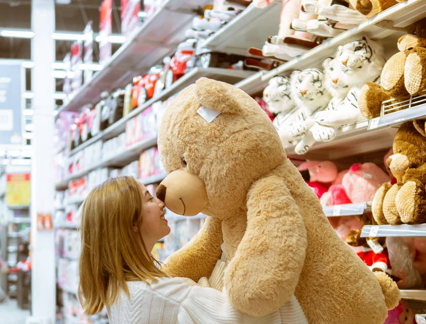 Mujer con un oso de peluche gigante en un pasillo en un negocio de juguetería.