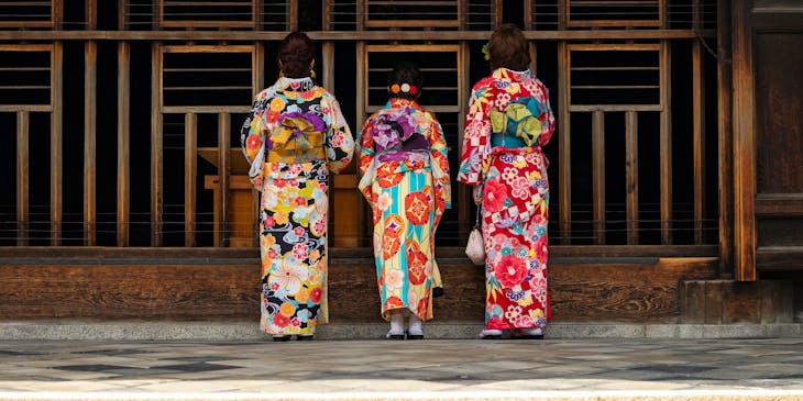 Three japanese women wearing their traditional clothing in front of the temple gate.