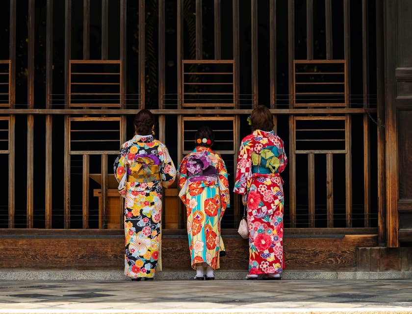 Três mulheres japonesas vestindo suas roupas tradicionais em frente ao portão de um templo.