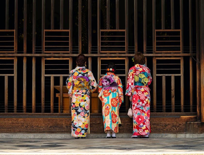 Three japanese women wearing their traditional clothing in front of the temple gate.