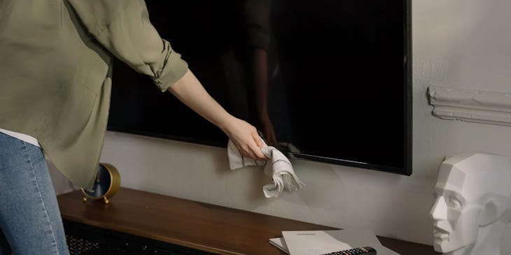 A woman cleaning a TV mounted on the wall.