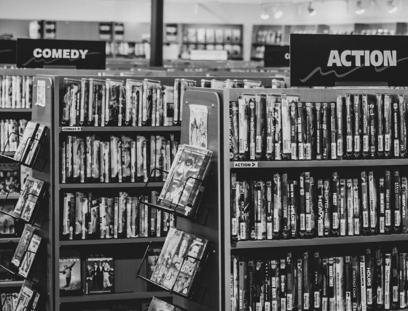 Un fotografía a blanco y negro de un estante con películas en un negocio de renta de películas y videojuegos.