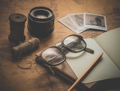 Occhiali vintage, un taccuino antico, delle polaroid e altri oggetti vintage sopra un tavolo.