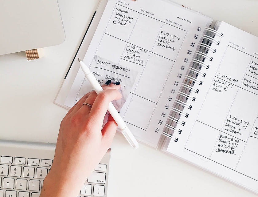 Un asistente virtual sosteniendo  una pluma sobre una agenda de planificación.