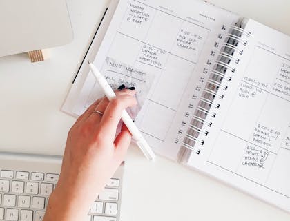 Assistente virtual segurando uma caneta em cima de uma agenda.