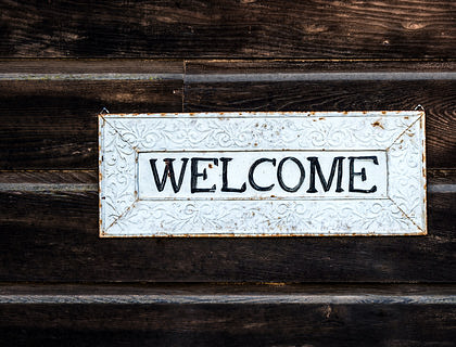 A white welcome sign on a dark wooden background greeting visitors.