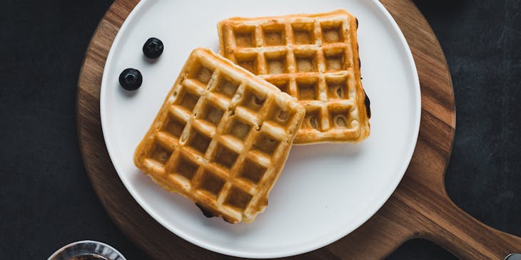 Two waffles on a white plate with blueberries.
