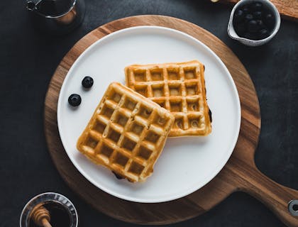 Dos waffles cuadrados sobre un plato blanco en una mesa negra.