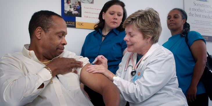 Woman injecting a man's arm at walk-in clinic.