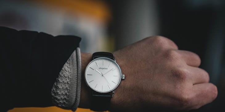 Watch with a leather strap and white face on someone's wrist.