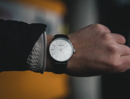 Watch with a leather strap and white face on someone's wrist.