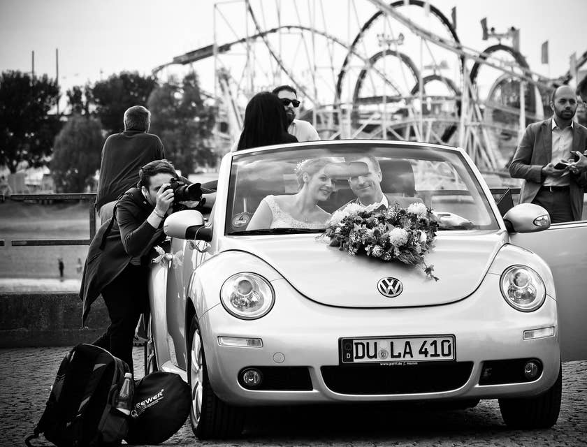 Un fotografo che sta scattando una foto a una coppia di sposi che si trovano nella loro macchina.