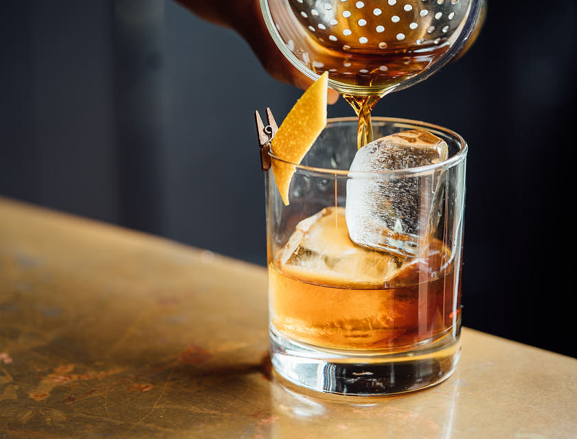 Un primo piano di una persona che versa whisky dentro ad un tumbler in un whisky bar.