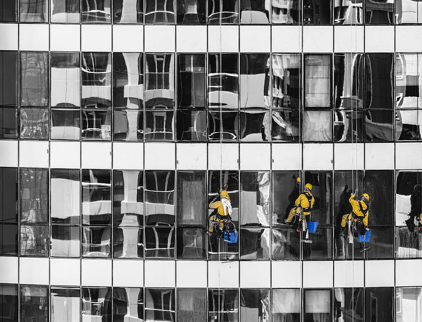 Fünf Fensterputzer seilen sich an einem Hochhaus ab, um die Glasfassade zu reinigen.