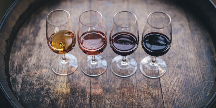 Wine glasses with small amounts of various wines in them, placed on a barrel.