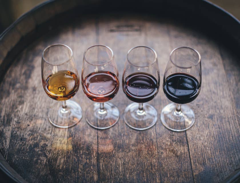 Wine glasses with small amounts of various wines in them, placed on a barrel.