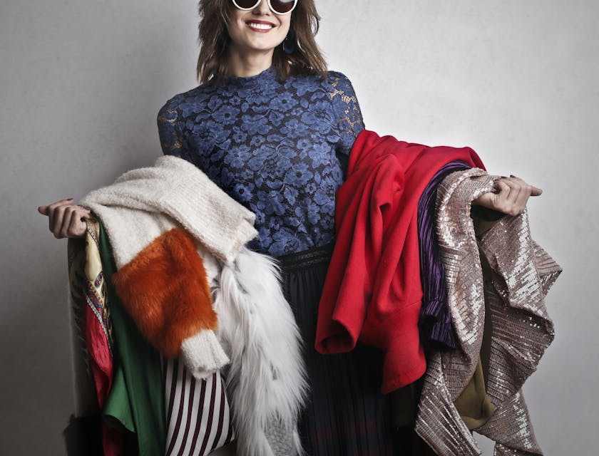 A woman wearing sunglasses holding a variety of clothing at a women's clothing business.