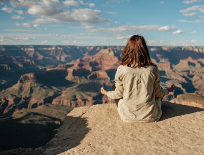 Mulher tendo um momento zen, sentada em uma montanha.