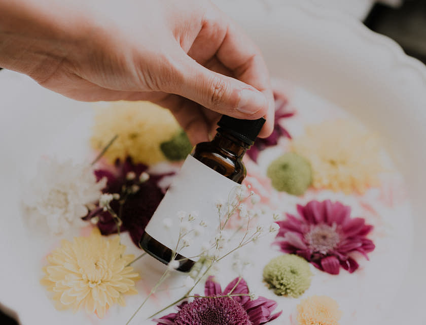 Pessoa segurando um frasco de óleo essencial sobre flores.