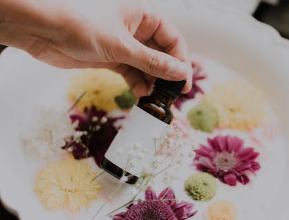 Une personne tenant une bouteille d'huile essentielle sur des fleurs.