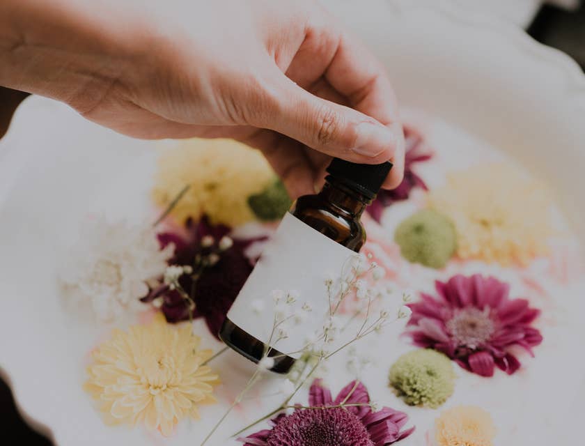 A person holding an essential oil bottle over flowers for naturopathic purposes.