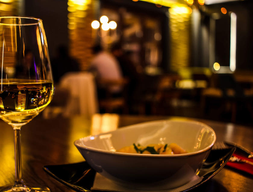 Un calice di vino bianco e un piatto sopra il tavolo di un'osteria.