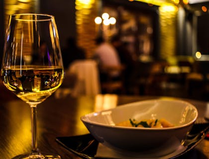 Un calice di vino bianco e un piatto sopra il tavolo di un'osteria.