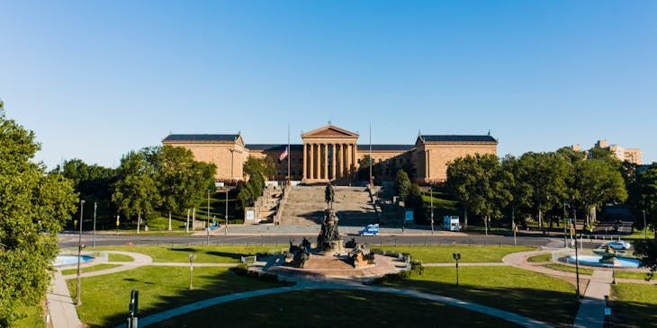 monument in the middle of a park with a huge building in the backdrop