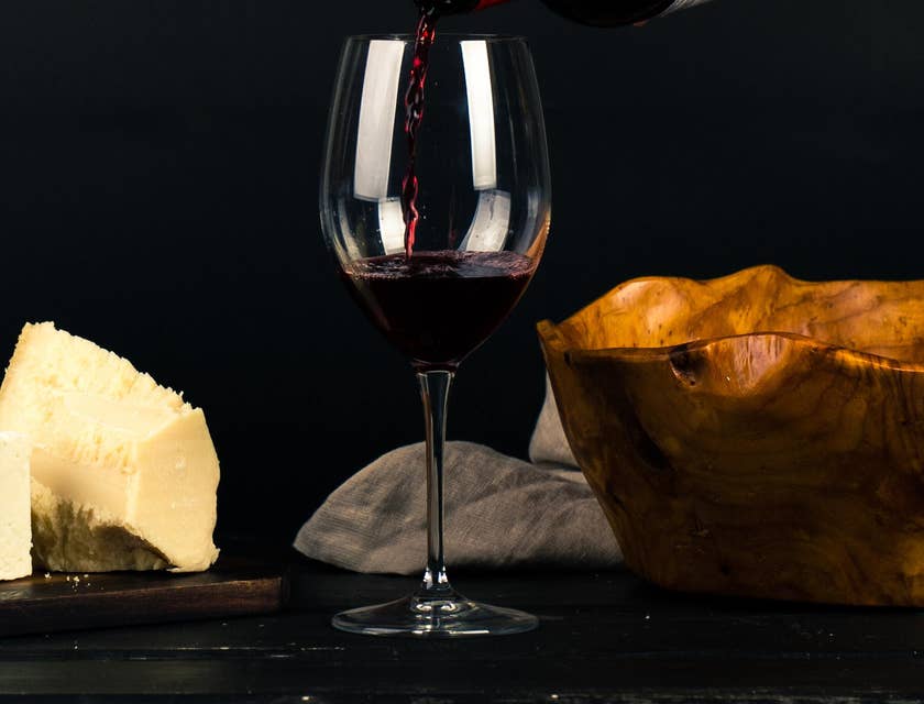 Ein Glas Rotwein steht in einer Weinstube neben Käse und Brot.