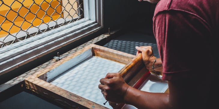 A man doing screen printing near a window.